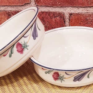 May include: Two white ceramic bowls with blue and green floral designs. The bowls have a blue rim and a white interior.