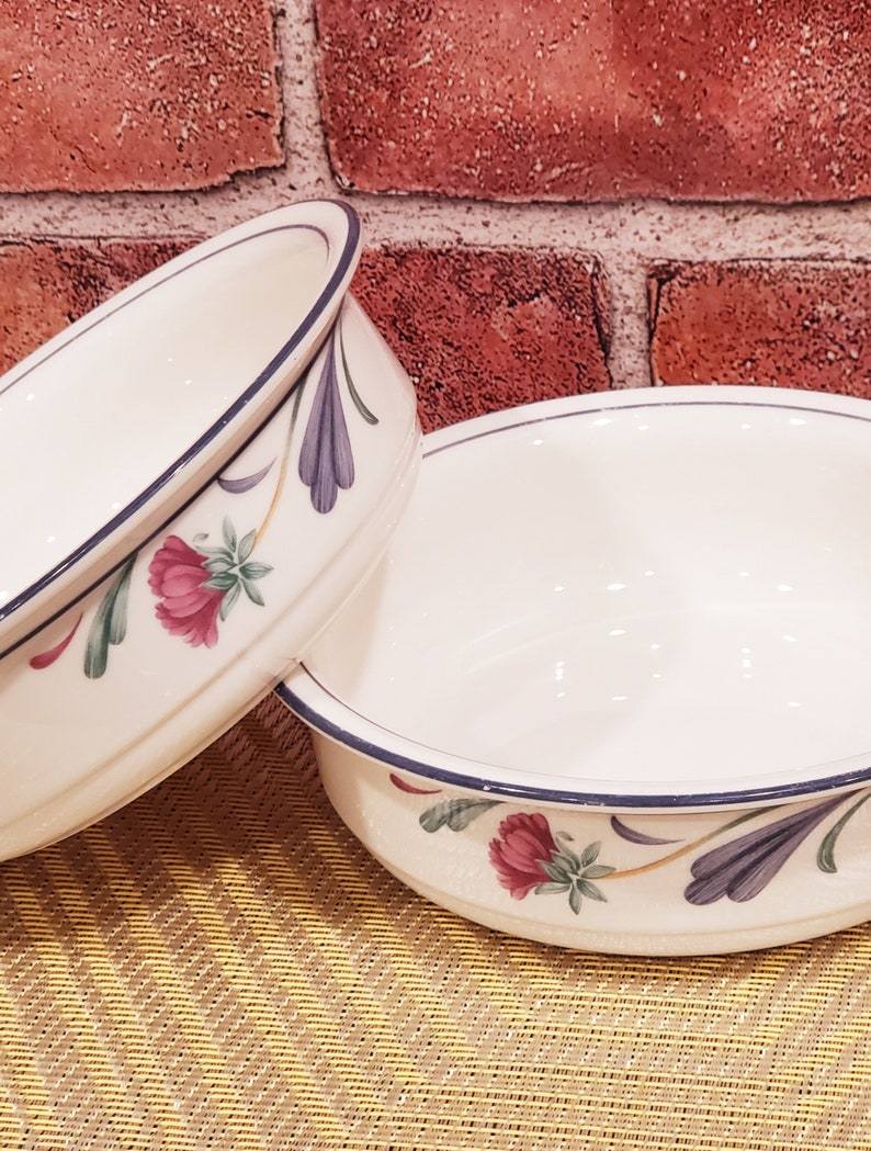 May include: Two white ceramic bowls with blue and green floral designs. The bowls have a blue rim and a white interior.
