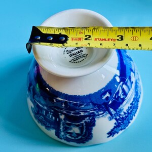 May include: A white and blue Spode Italian teacup, with a blue scenic design. The teacup is measured with a yellow tape measure, showing a diameter of approximately 2 inches.
