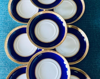 May include: A set of nine circular saucers arranged in a grid. Each saucer features a white center, a wide cobalt blue rim, and a decorative gold-toned metallic edge. The saucers are uniform in design, showcasing a classic round shape.