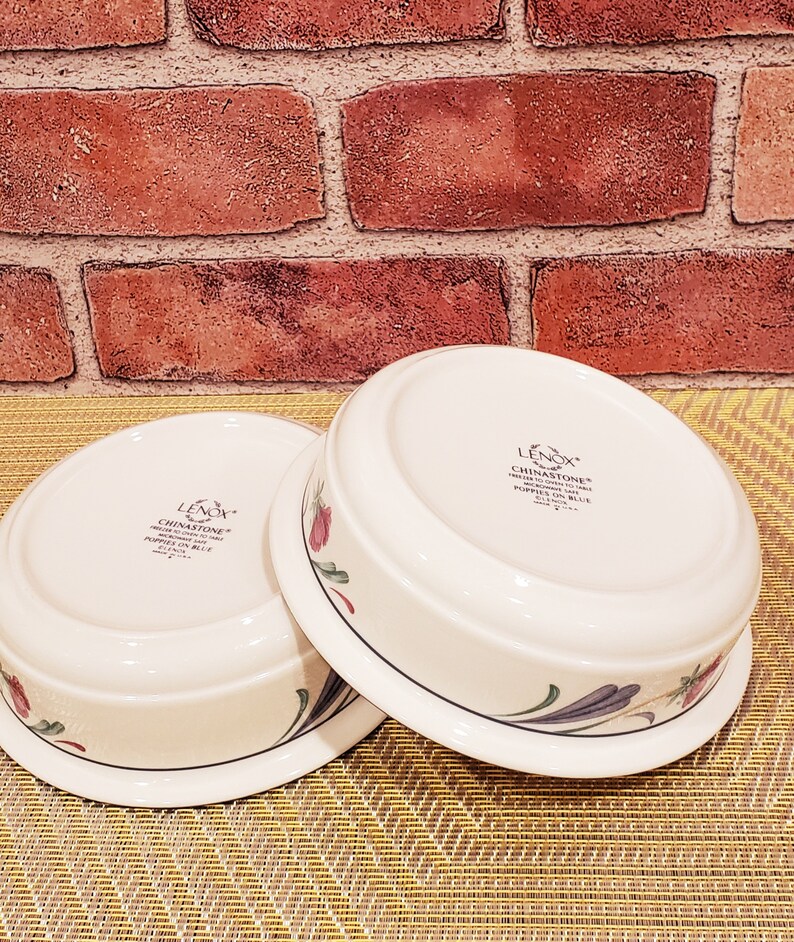 May include: Two white ceramic bowls with floral designs. The bowls are made by Lenox and are part of the Chinastone Poppy's in Blue collection.