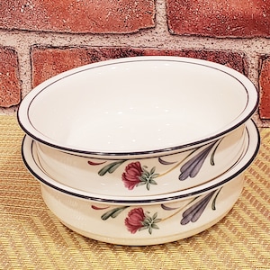 May include: Two white ceramic bowls with a floral design. The bowls have a black rim and feature a blue and green floral pattern with pink flowers.