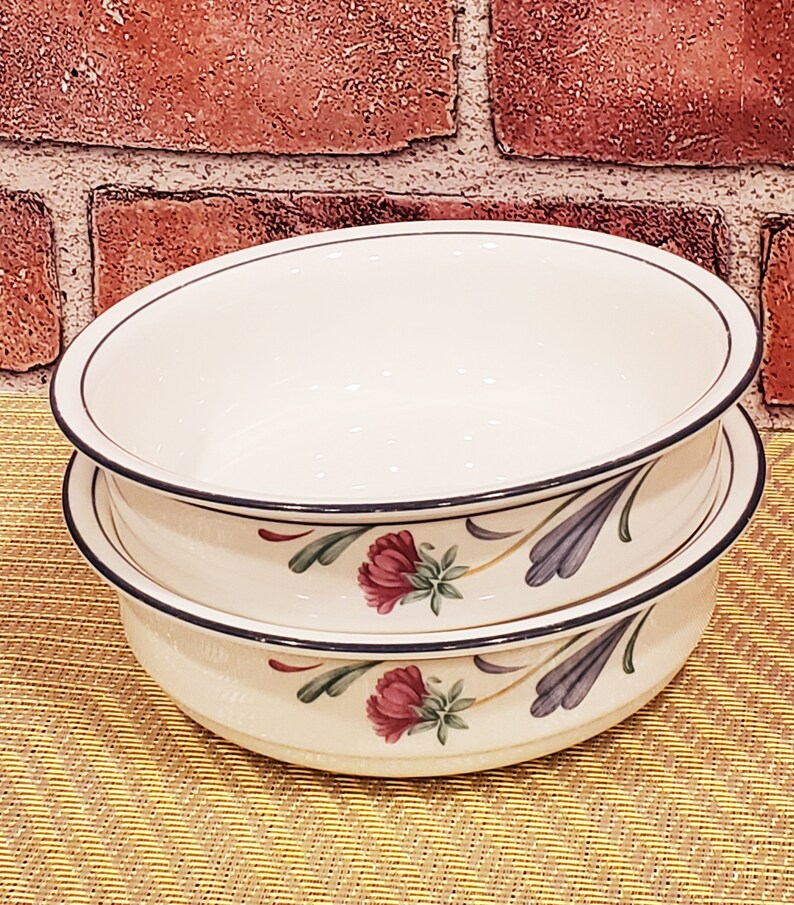 May include: Two white ceramic bowls with a floral design. The bowls have a black rim and feature a blue and green floral pattern with pink flowers.