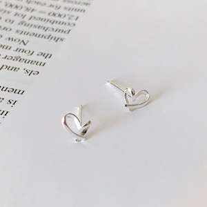 May include: A pair of silver heart-shaped stud earrings. The earrings are simple and delicate, with a minimalist design.