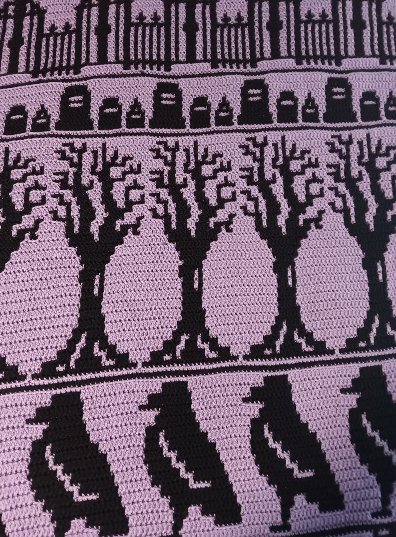 May include: Crocheted blanket with a purple background and black details. The design features a graveyard scene with a fence, tombstones, trees, and crows.