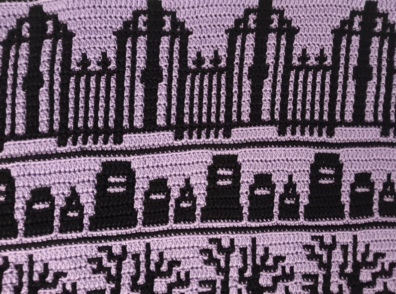 May include: A close-up of a crocheted blanket with a purple background and black details. The design features a repeating pattern of gates, tombstones, and trees, creating a spooky and whimsical Halloween theme.