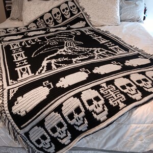May include: A black and white crocheted throw blanket with a skull pattern. The blanket features a large skull design in the center and smaller skulls along the edges. The blanket is made with a soft, textured yarn.
