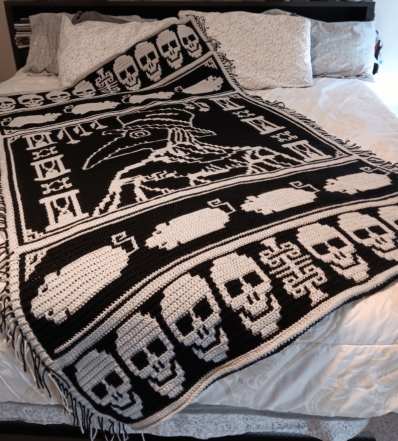 May include: A black and white crocheted throw blanket with a skull pattern. The blanket features a large skull design in the center and smaller skulls along the edges. The blanket is made with a soft, textured yarn.