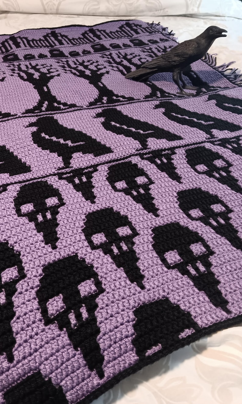 May include: A purple crocheted blanket with a black skull pattern and a black crow figurine on top.