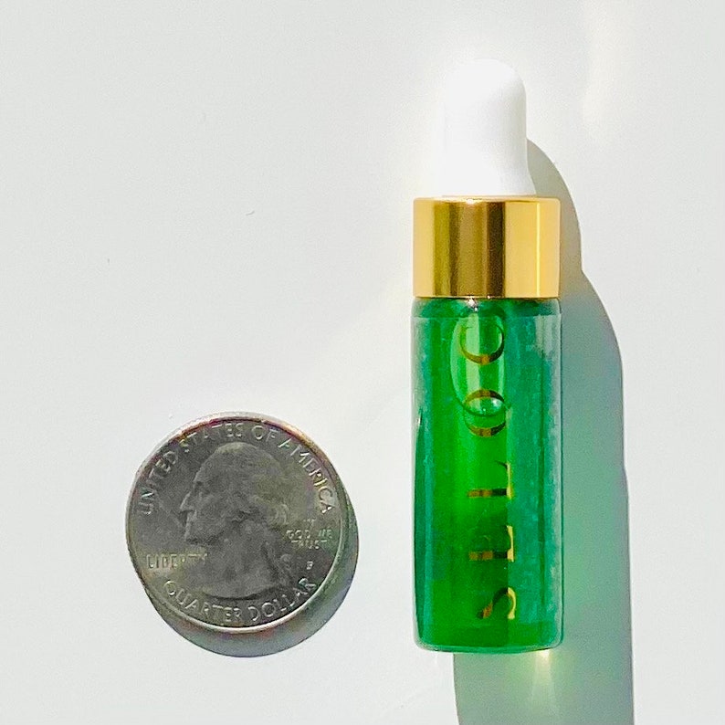 K&ouml;nnte beinhalten: Eine kleine gr&uuml;ne Glasflasche mit goldenem Deckel und einem wei&szlig;en Tropfer. Die Flasche ist mit "Coco" in goldenen Buchstaben beschriftet.