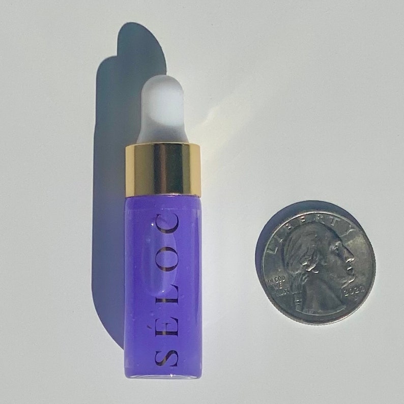 Pu&ograve; includere: Un piccolo flacone di vetro viola con un tappo dorato e un contagocce bianco. Il flacone &egrave; etichettato "SELOC" in lettere bianche. Il flacone &egrave; accanto a una moneta da un quarto di dollaro americano per riferimento alle dimensioni.
