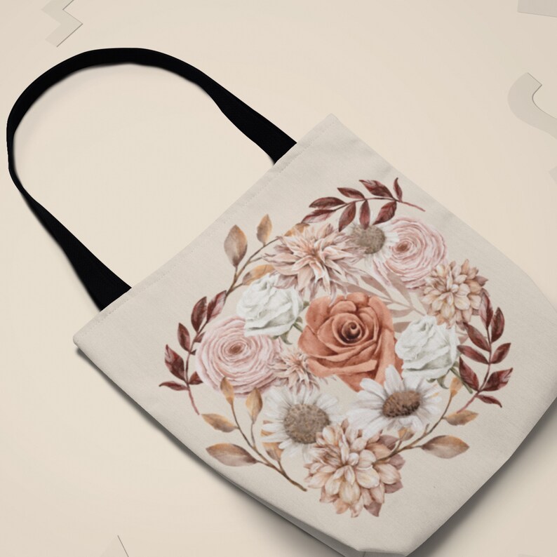 May include: A beige tote bag with a black handle features a watercolour floral design. The design includes a variety of flowers in shades of pink, white, and brown, with leaves in shades of brown and green.