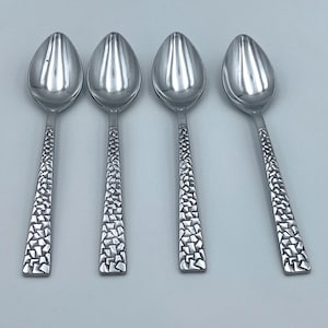 May include: Four silver-colored metal spoons arranged in a row. Each spoon features a smooth, polished oval bowl and a flat handle decorated with a textured, mosaic-like pattern of small, irregular geometric shapes across the entire length.