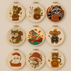 Puede incluir: Una colección de doce aros bordados con diseños de temática otoñal. Cada aro presenta un personaje o escena caprichosa diferente, incluyendo un murciélago, una ardilla y un mapache, sobre un fondo crema. Los aros están enmarcados en madera natural.