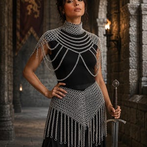 May include: A silver chainmail shoulder piece and matching waist belt featuring intricate interlocking metal rings and dangling chain fringe. The shoulder piece has a high neck collar design, while the waist belt forms a pointed front panel.
