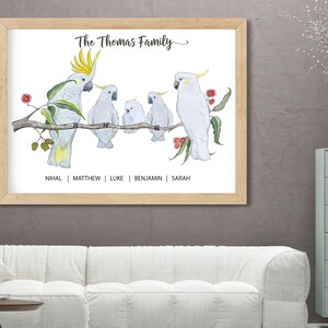Pu&ograve; includere: Una stampa incorniciata con un'illustrazione ad acquerello di cacatua bianchi su un ramo. Il testo "The Thomas Family" &egrave; sopra gli uccelli, con i nomi sotto. La cornice &egrave; marrone chiaro.