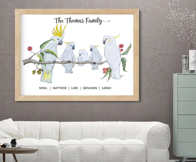 Pu&ograve; includere: Una stampa incorniciata con un'illustrazione ad acquerello di cacatua bianchi su un ramo. Il testo "The Thomas Family" &egrave; sopra gli uccelli, con i nomi sotto. La cornice &egrave; marrone chiaro.