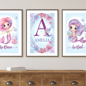 May include: Three framed prints with a mermaid theme. The left print features a pink mermaid with the text "be brave". The middle print features a purple letter "A" with the name "Amelia" and a small mermaid. The right print features a purple mermaid with the text "be kind".