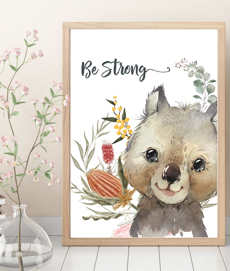 May include: A watercolor illustration of a cute wombat with a floral wreath around its head. The text "Be Strong" is written above the wombat. The background is white.
