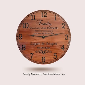 May include: A wooden clock with a brown wood grain finish. The clock face has black Roman numerals and a quote that reads "Family, where today's little moments become tomorrow's precious memories". The clock also has the names "Logan & Megan" and the date "03-30-2024" engraved on it.