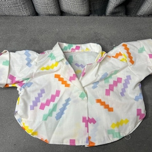 May include: A white button-up shirt with a colourful geometric pattern. The pattern features pink, blue, green, yellow, and orange zigzags.