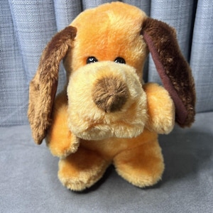 May include: A plush brown and tan dog toy with brown ears. The dog has a brown nose and black eyes.