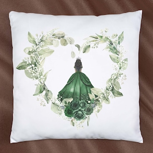 K&ouml;nnte beinhalten: Ein wei&szlig;es Kissen mit einem gr&uuml;nen Blumendesign, das eine Frau in einem gr&uuml;nen Kleid und einer Krone zeigt. Das Blumendesign hat die Form eines Herzens.