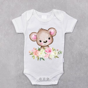 May include: White baby onesie with a brown bear with pink ears and a floral design in shades of pink, white, and green.