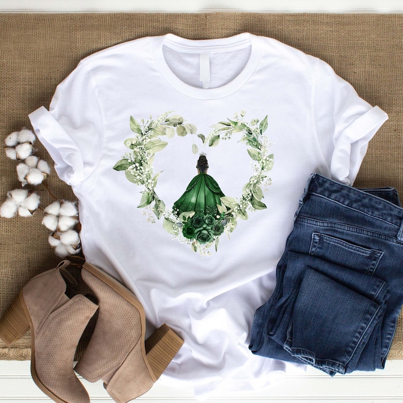 K&ouml;nnte beinhalten: Wei&szlig;es T-Shirt mit einem gr&uuml;nen floralen Herzdesign, das eine Frau in einem gr&uuml;nen Kleid zeigt. Das Design ist mittig auf dem Shirt platziert.