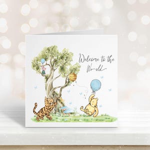 May include: A greeting card with a watercolor illustration featuring Winnie the Pooh characters. The card has a tree, a tiger, and a bear holding a blue balloon. The text "Welcome to the World" is written in cursive.