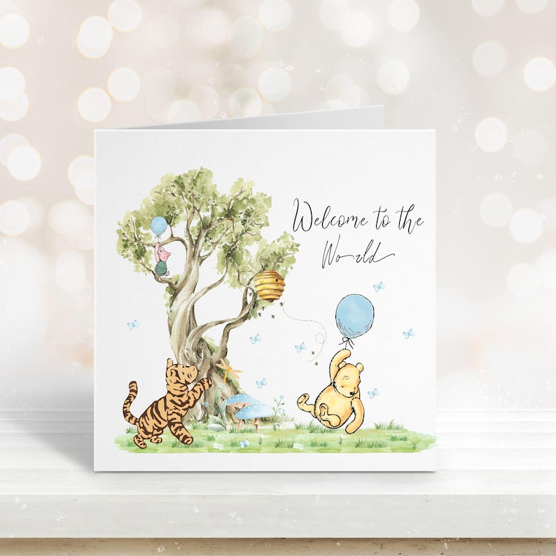 May include: A greeting card with a watercolor illustration featuring Winnie the Pooh characters. The card has a tree, a tiger, and a bear holding a blue balloon. The text "Welcome to the World" is written in cursive.