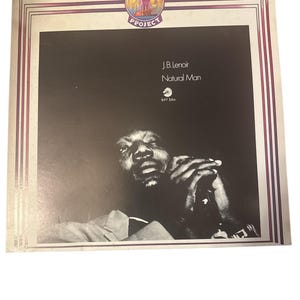 May include: Album cover for J.B. Lenoir's "Natural Man" from the Blues & Rock Project. The album art features a black and white photo of a man with his hands clasped. The album title and artist are printed in white.
