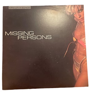 May include: A black vinyl record cover with the text "MINI LP/4 SONGS" and "MISSING PERSONS" in white. The cover features a woman with blonde hair wearing a pink and yellow bikini.