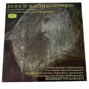 May include: A vintage record album cover featuring a black and white portrait of a man with the title "J.S. BACH MATTHÄUS-PASSION" in yellow text. The album cover also includes the text "ST. MATTHEW PASSION" and "LA PASSION SELON SAINT MATTHIEU" in yellow text. The album cover lists the performers: Gundula Janowitz, Christa Ludwig, Peter Schreier, Horst R. Laubenthal, Dietrich Fischer-Dieskau, Walter Berry, Anton Diakov, Wiener Singverein, Berliner Philharmoniker, and Herbert von Karajan.