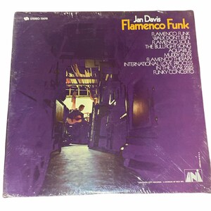 May include: A purple vinyl record album cover with the title "Jan Davis Flamenco Funk" and a list of songs including "Flamenco Funk", "Walk Don't Run", "Flamenco Soul", "The Bullfight Song", "Aquarius", "Muddy River", "Flamenco Therapy", "International Love Process", "In The Year 2525", and "Funky Concerto". The cover features a photo of a man playing a guitar in a hallway.