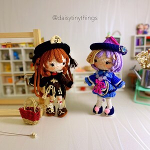 Puede incluir: Dos mu&ntilde;ecas de crochet que llevan sombreros y vestidos. La mu&ntilde;eca de la izquierda lleva un sombrero marr&oacute;n y un vestido marr&oacute;n con un cuello blanco. La mu&ntilde;eca de la derecha lleva un sombrero azul y un vestido azul con un lazo rosa. Las mu&ntilde;ecas est&aacute;n de pie sobre una superficie blanca. @daisytinythings