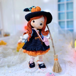 May include: A crocheted witch doll wearing a black hat with an orange pumpkin on top, a black and orange dress, and white stockings. The doll is holding a small pink bag and a broom.