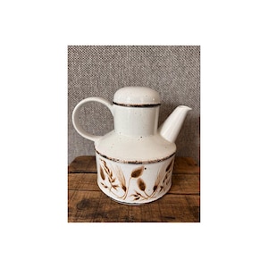 May include: A white ceramic teapot with a lid, handle, and spout. The teapot has a brown floral design around the base and a brown trim. The teapot is sitting on a wooden surface.