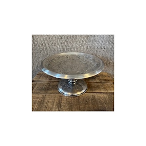 May include: A silver cake stand with an ornate, embossed design. The stand has a round base and a circular top.