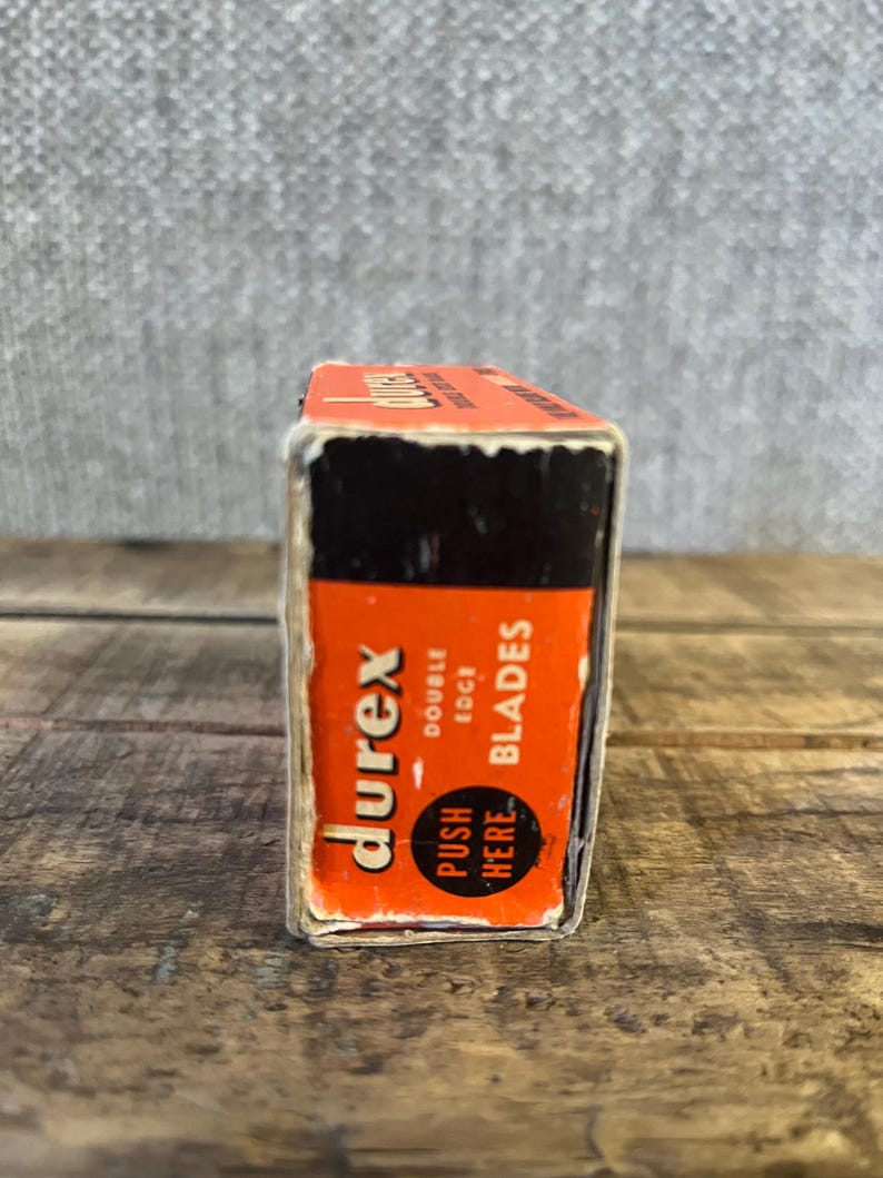 May include: A vintage box of Durex double edge blades. The box is orange with black accents and features the Durex logo and the words "double edge blades". The text "push here" is also visible on the box.