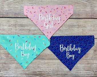 May include: Four dog bandanas with a sprinkle pattern. Two bandanas are blue with white text that says "Birthday Boy". One bandana is pink with white text that says "Birthday Girl". One bandana is teal with white text that says "Birthday Boy".