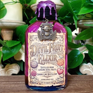 May include: A purple glass bottle labeled "Devil Fruit Elixir" with a decorative metal emblem. The bottle has a black cap with purple dripping wax. The label includes text and illustrations of various fruits. The bottle contains 200 ml of liquid and is 80% alcohol.