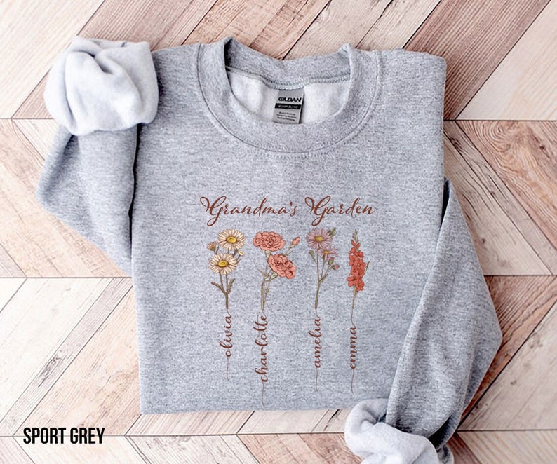 May include: A gray sweatshirt with the text "Grandma's Garden" and four flowers with names written below them: Olivia, Charlotte, Amelia, Emma.