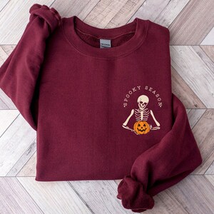 May include: Burgundy sweatshirt with a skeleton holding a pumpkin and the text "Spooky Season".