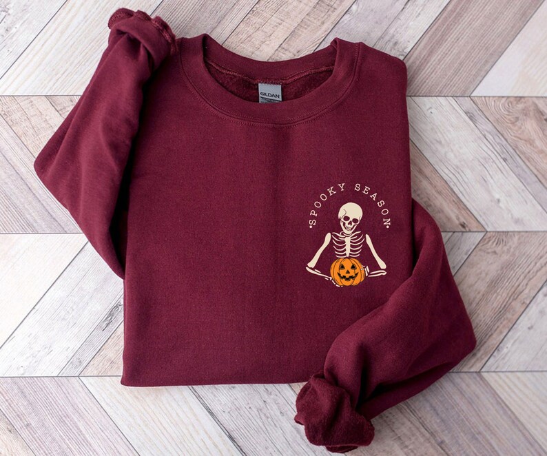 May include: Burgundy sweatshirt with a skeleton holding a pumpkin and the text "Spooky Season".