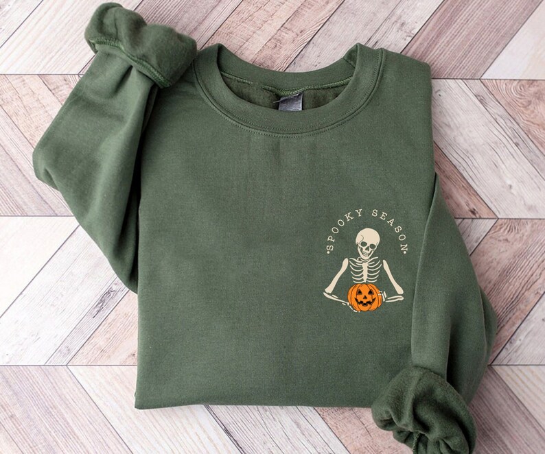 May include: A dark green sweatshirt with a white graphic of a skeleton holding a jack-o'-lantern. The graphic says "Spooky Season".