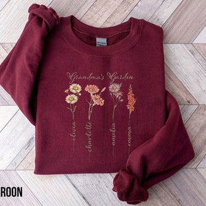 May include: Maroon sweatshirt with the text "Grandma's Garden" and a floral design. The names Olivia, Charlotte, Amelia, and Emma are written below the flowers.