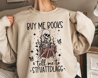 May include: A beige sweatshirt with a skeleton reading a book and the text "BUY ME BOOKS & TELL ME TO STFUATTDLAGG".