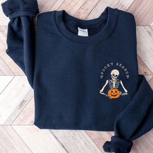 May include: A navy blue sweatshirt with a white graphic of a skeleton holding a pumpkin. The graphic says "Spooky Season".