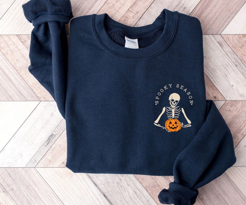 May include: A navy blue sweatshirt with a white graphic of a skeleton holding a pumpkin. The graphic says "Spooky Season".